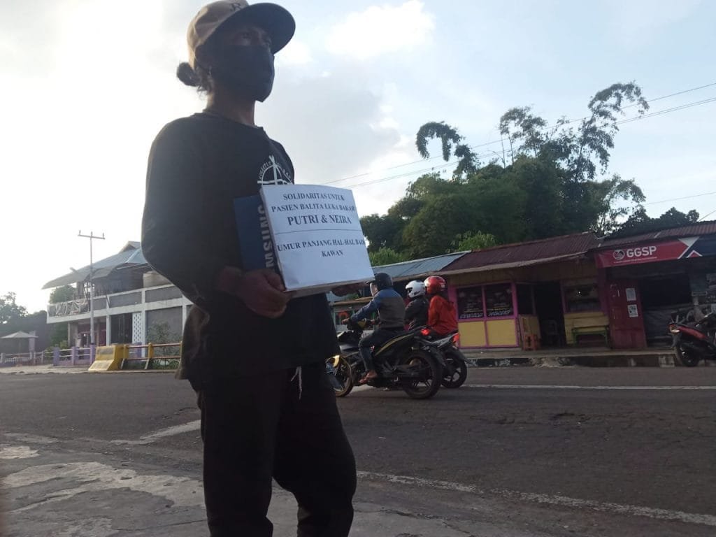 Seorang pemuda sedang melakukan penggalangan dana untuk biaya Rumah Sakit dua bocah pasien luka bakar asal Manggarai Barat. Foto: Istimewa